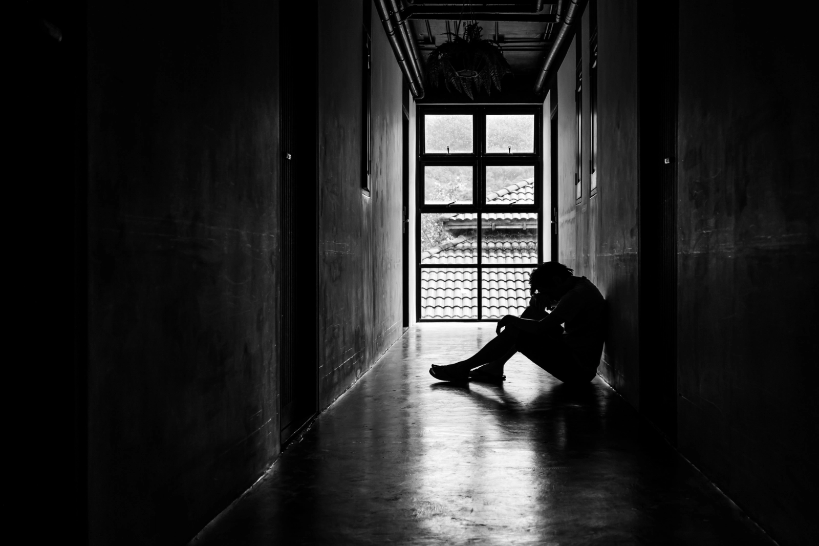 Trauma and Addiction: A dark hallway with a person sitting against a wall looking down